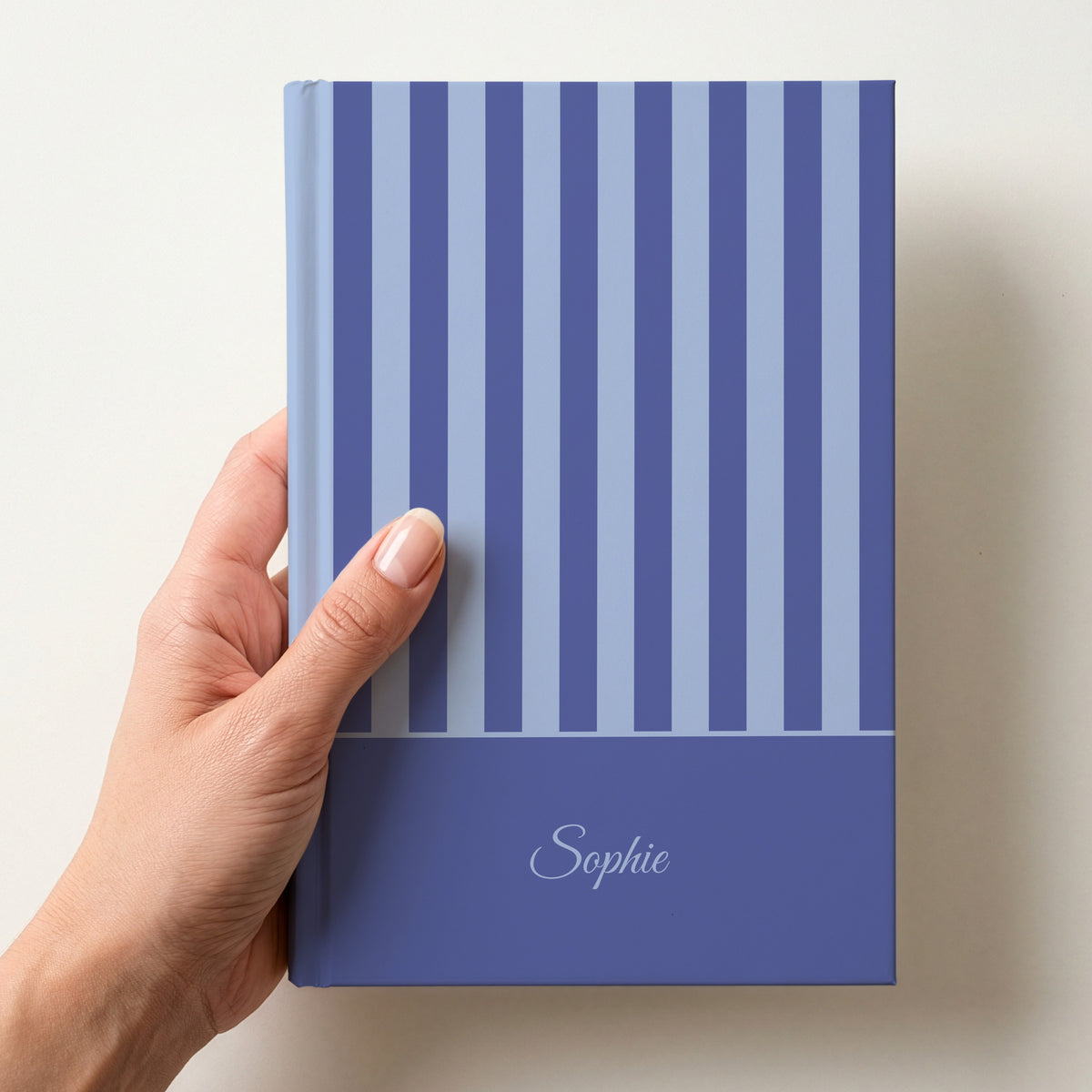 Hand holding a personalised blue striped notebook with a dark blue band and the name Sophie in script
