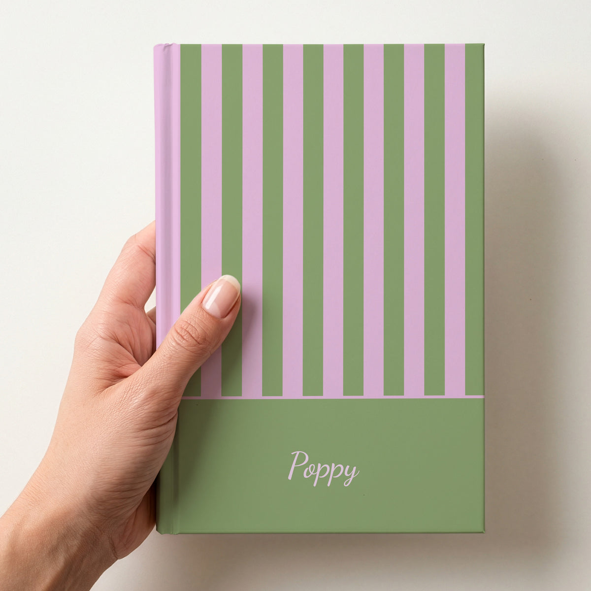 Hand holding a personalised green and pink strawberry matcha striped notebook with the name Poppy