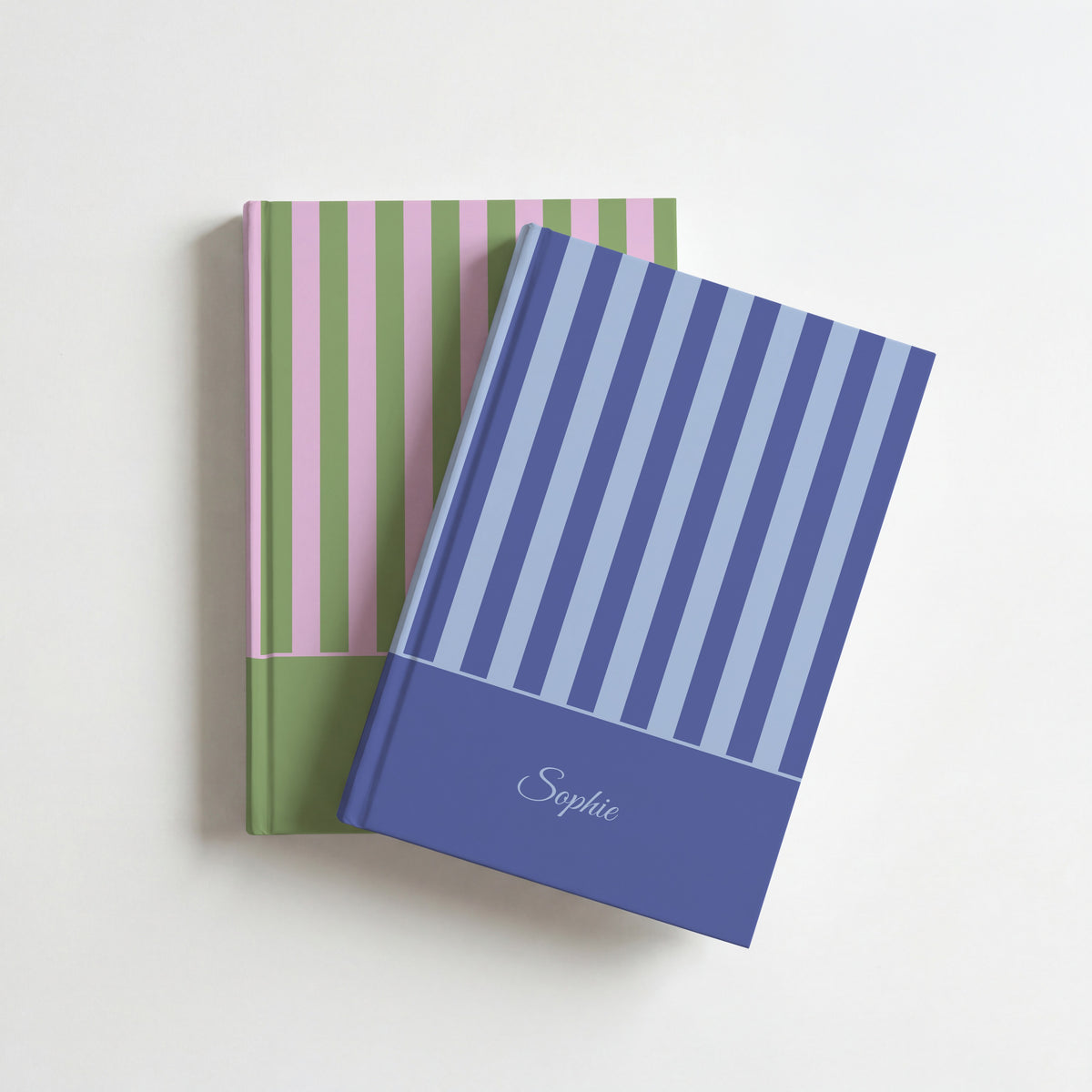 Two personalised striped notebooks, blue with the name Sophie on top of green and pink strawberry matcha