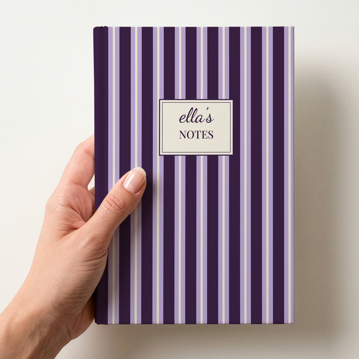 Hand holding a personalised plum and lilac striped notebook with a label reading ella's Notes in script
