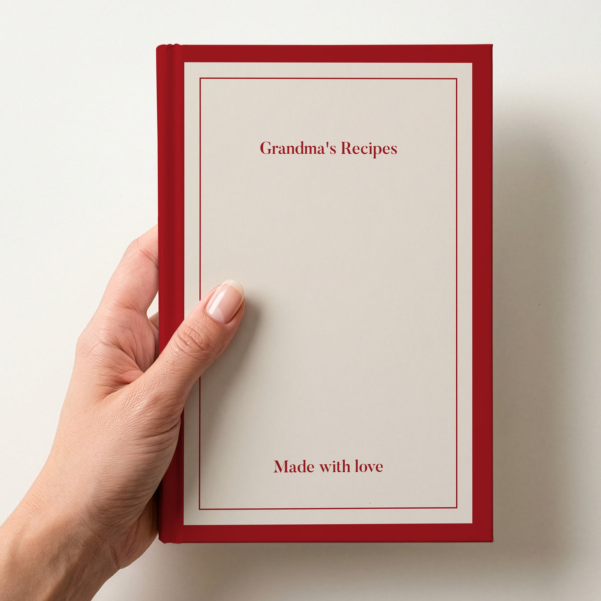 Hand holding a personalised cream notebook with a red border reading Grandma's Recipes and Made with love