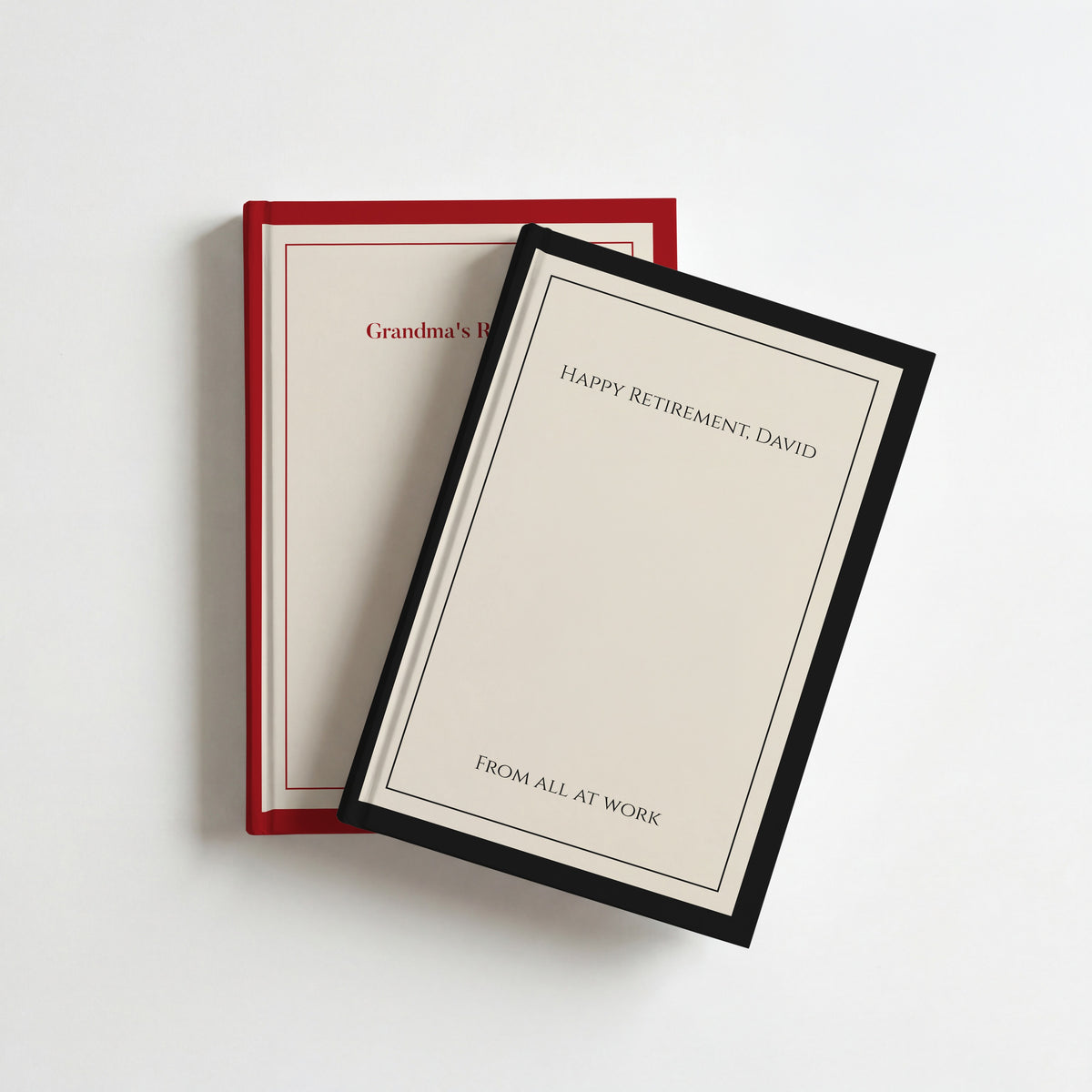 Two personalised classic border notebooks, black and cream reading Happy Retirement, David on top of red and cream Grandma's Recipes