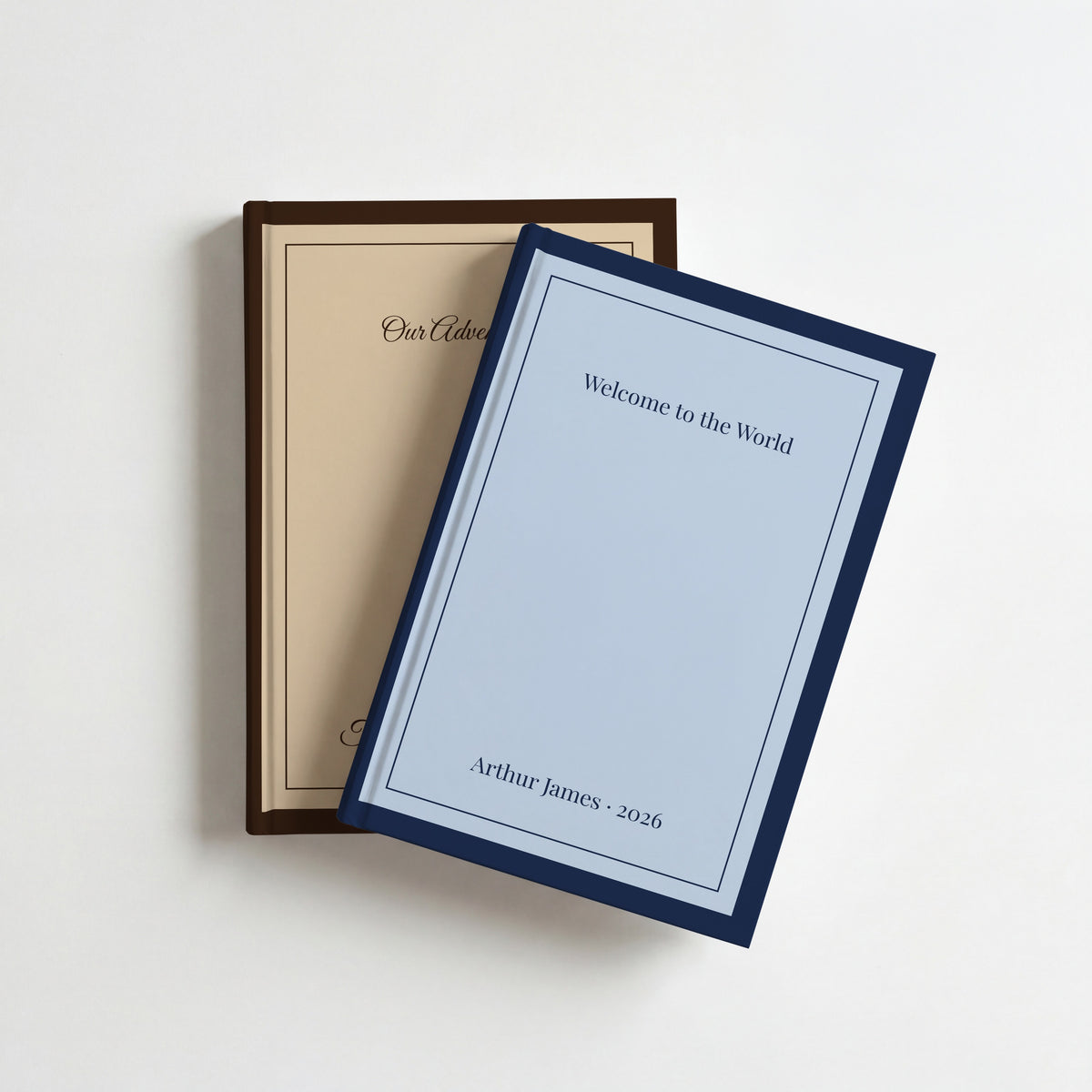 Two personalised classic border notebooks, navy and sky reading Welcome to the World on top of chocolate and caramel