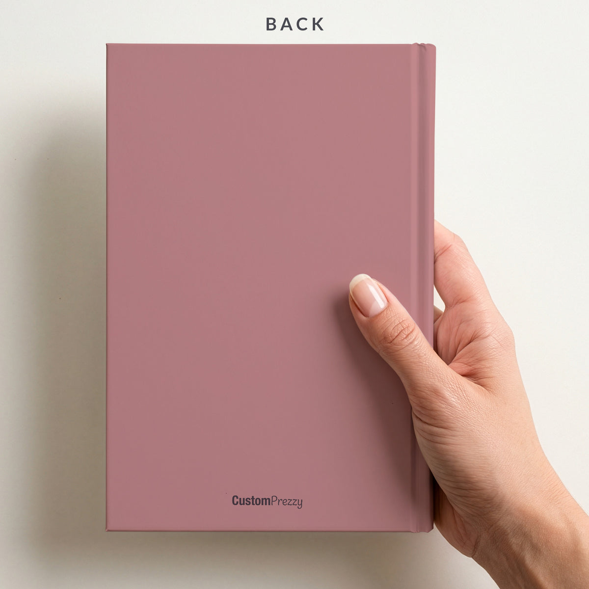 Back of the dusty rose notebook held in a hand, with the Custom Prezzy wordmark at the foot