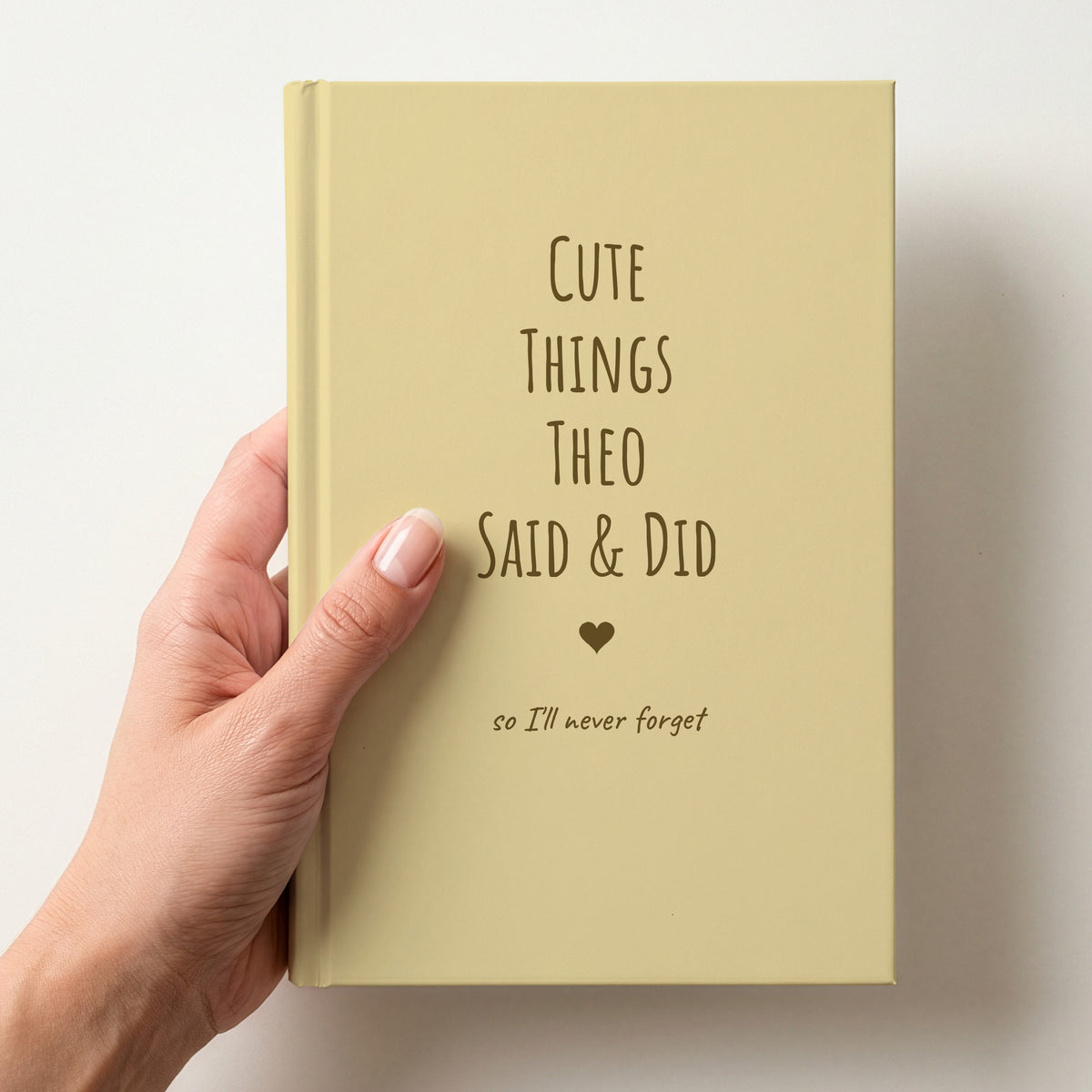 Hand holding a butter yellow personalised journal with brown lettering reading Cute Things Theo Said & Did