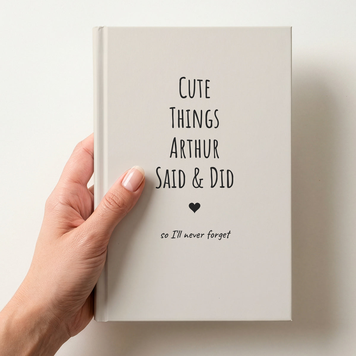Hand holding a cream personalised journal with charcoal lettering reading Cute Things Arthur Said & Did