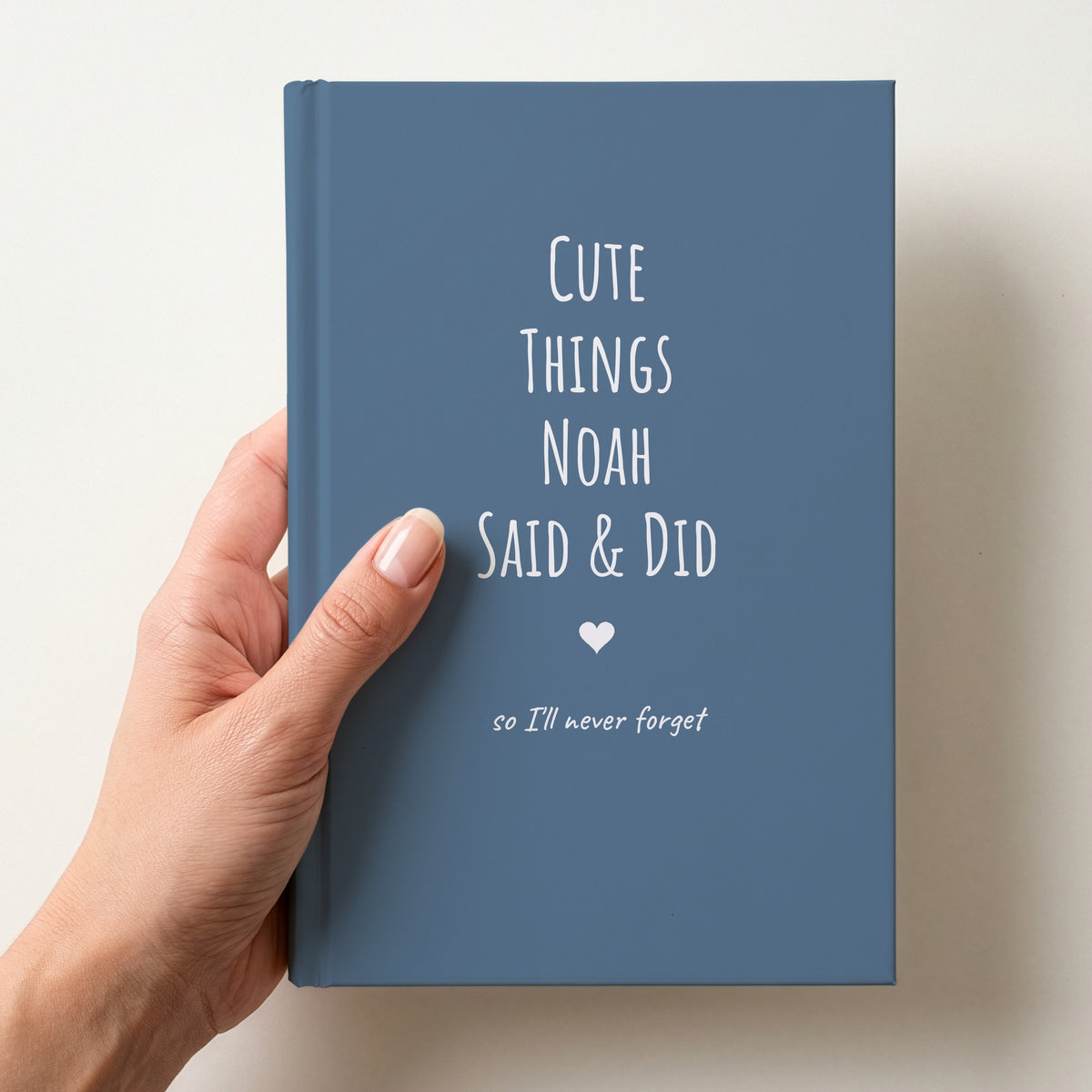 Hand holding a dusty blue personalised journal reading Cute Things Noah Said & Did, so we'll never forget