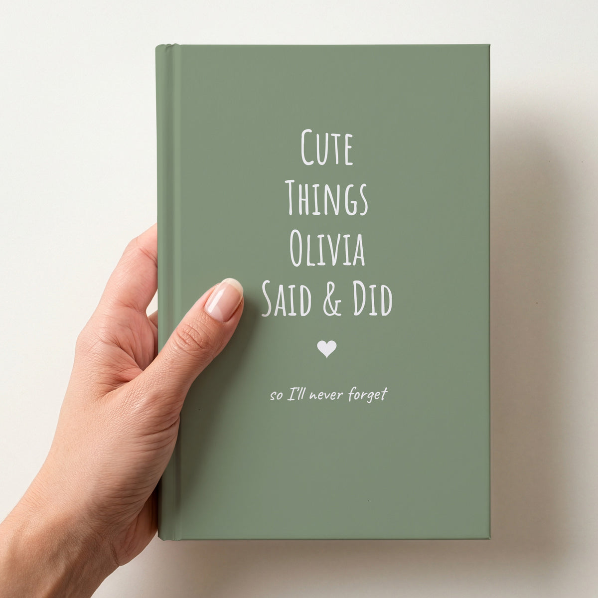 Hand holding a sage green personalised journal reading Cute Things Olivia Said & Did, with a heart and so I'll never forget