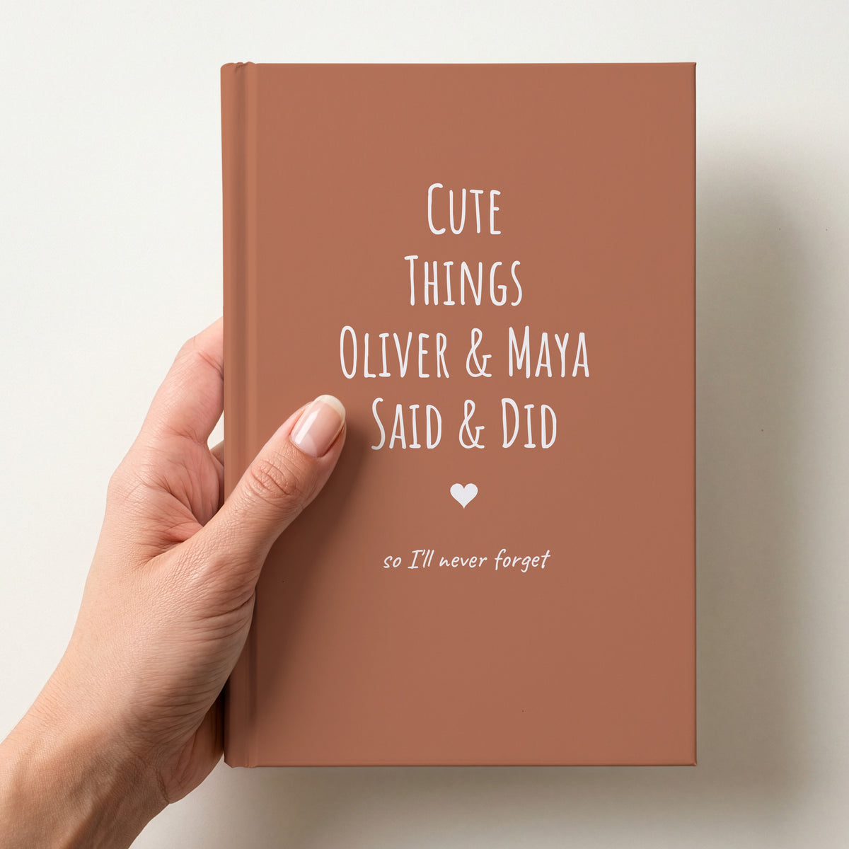 Hand holding a terracotta personalised journal reading Cute Things Oliver & Maya Said & Did, so we'll never forget