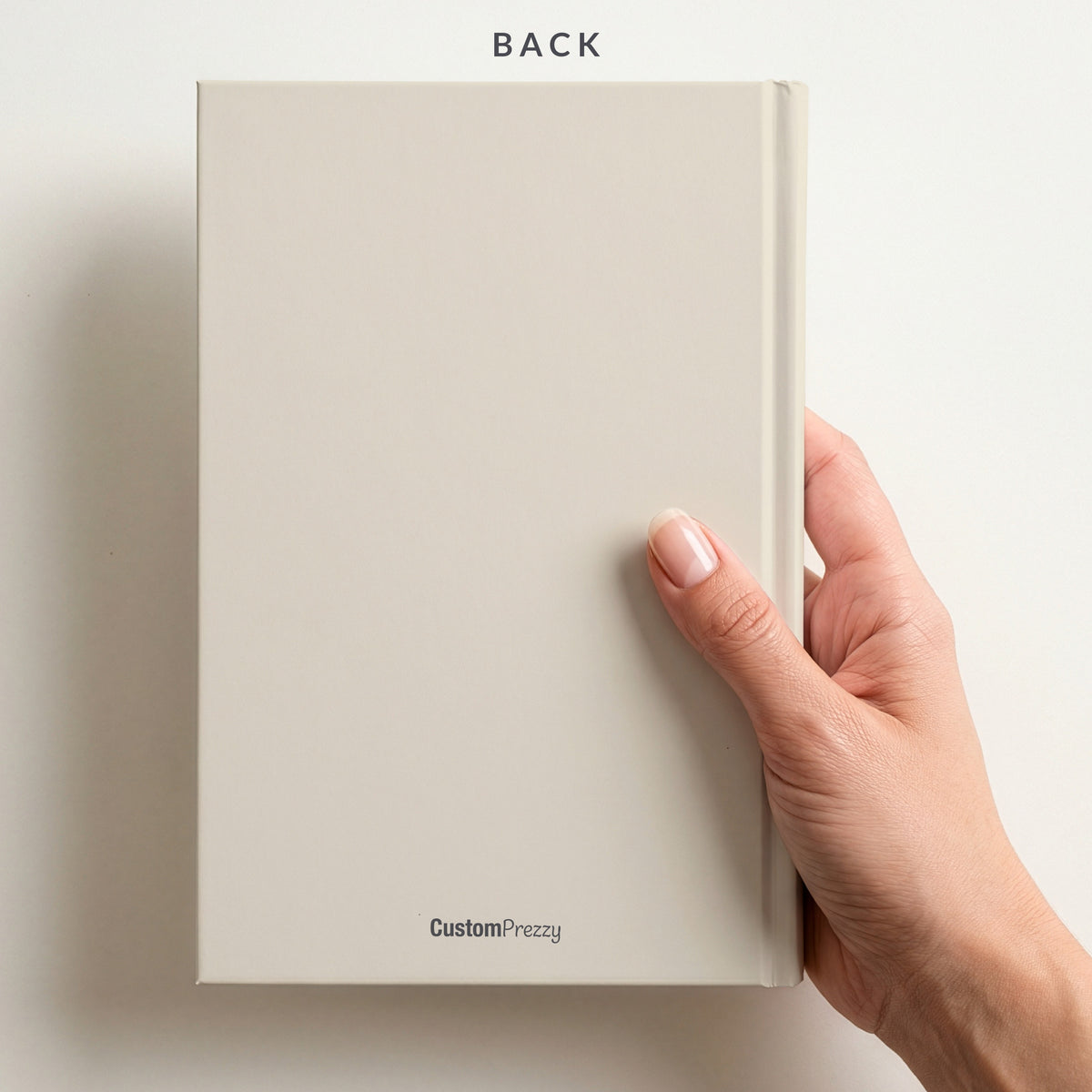 Back of the ivory rainbow notebook held in a hand, with the Custom Prezzy wordmark at the foot