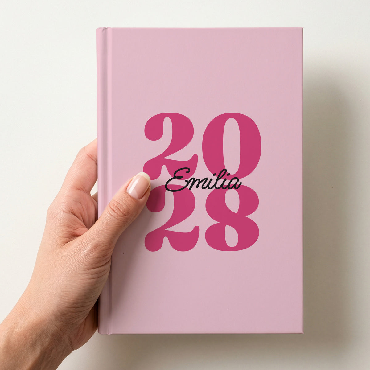 Hand holding a blush pink personalised journal with raspberry 2028 numbers and the name Emilia