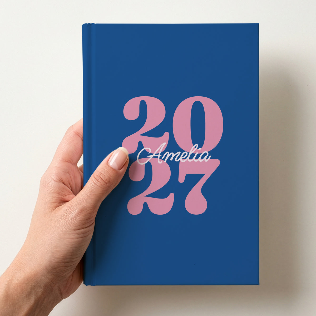 Hand holding a cobalt blue personalised journal with big pink 2027 numbers and the name Amelia in white script