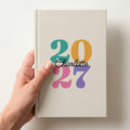 Hand holding an ivory personalised journal with rainbow 2027 numbers and the name Charlotte in script