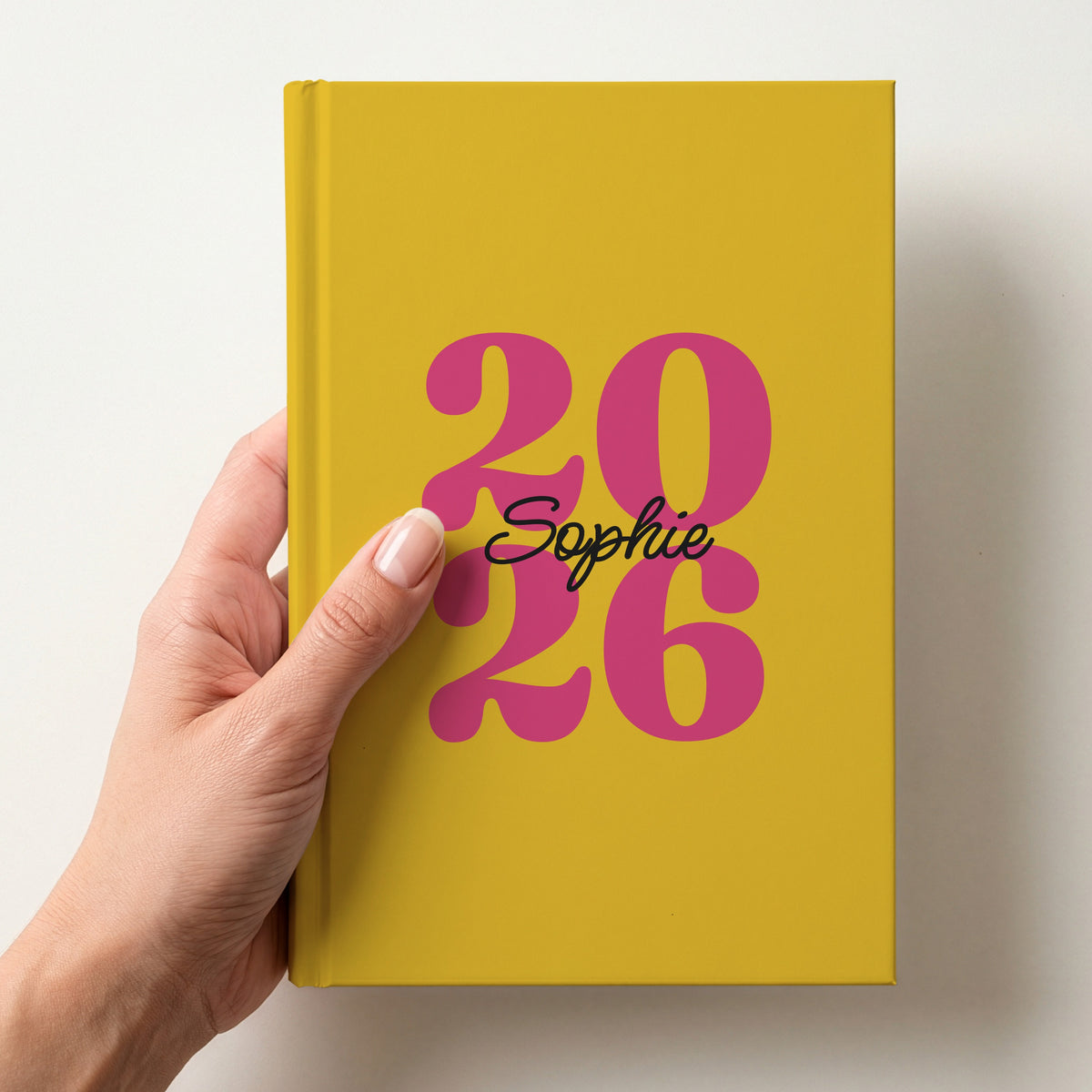 Hand holding a mustard yellow personalised journal with pink 2026 numbers and the name Sophie