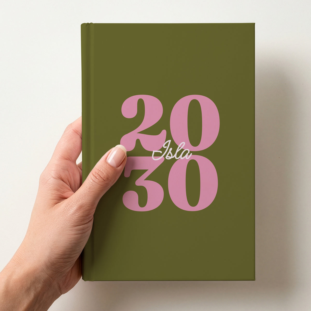 Hand holding an olive green personalised journal with pink 2030 numbers and the name Isla