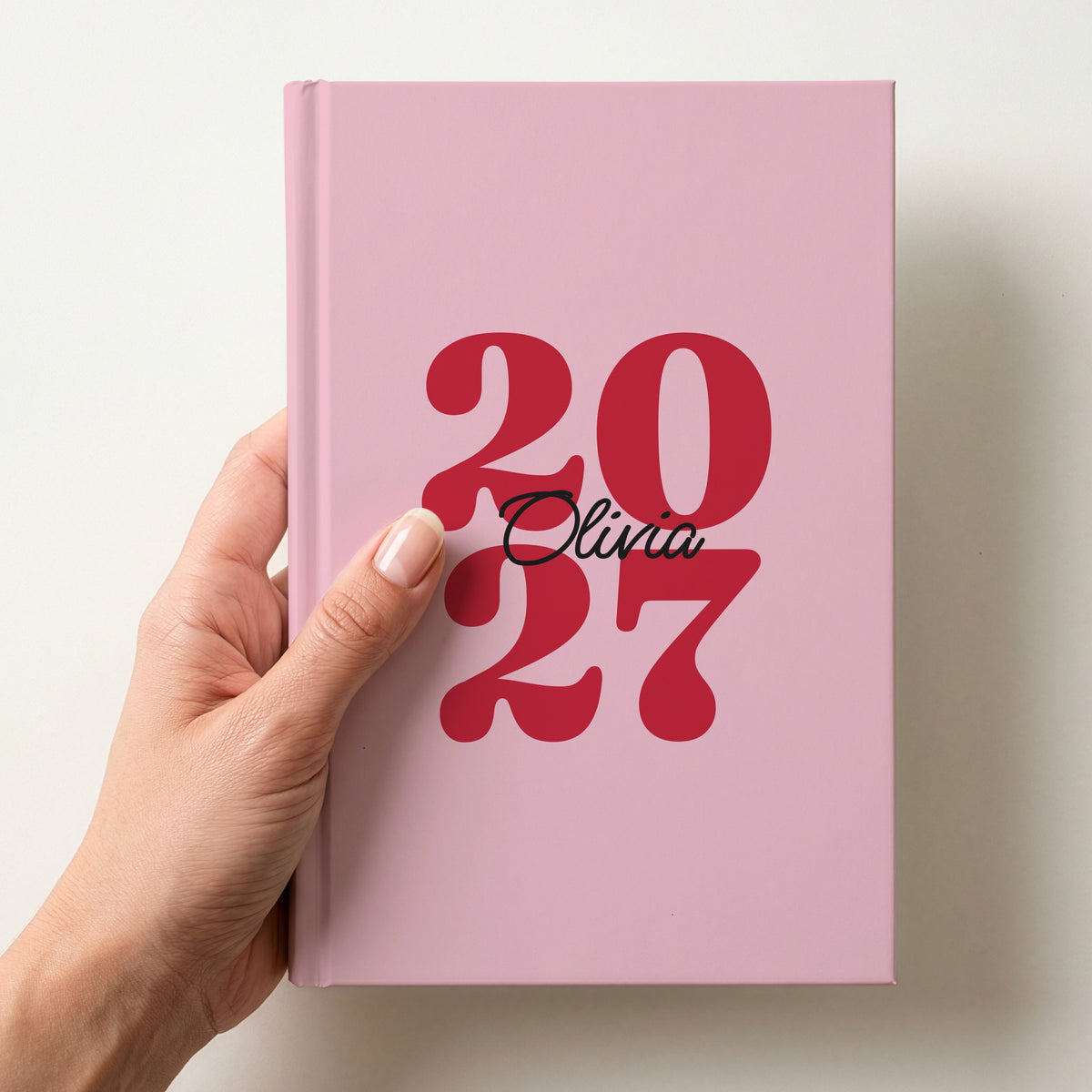 Hand holding a pink personalised journal with red 2027 numbers and the name Olivia