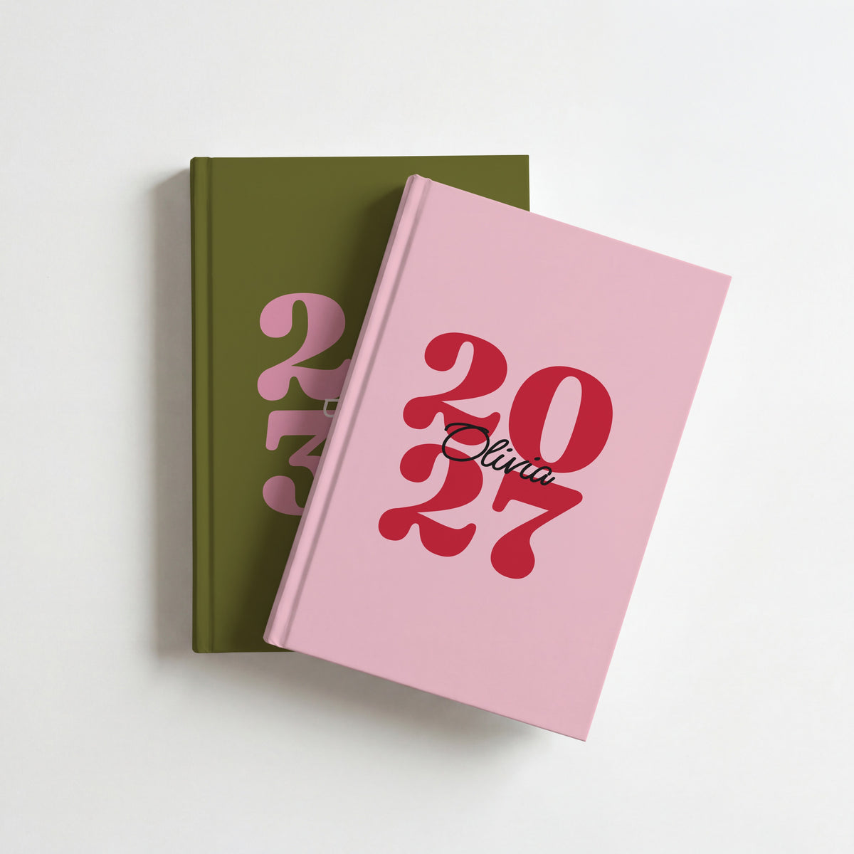 Two personalised year journals, pink and red 2027 for Olivia on top of olive green 2030