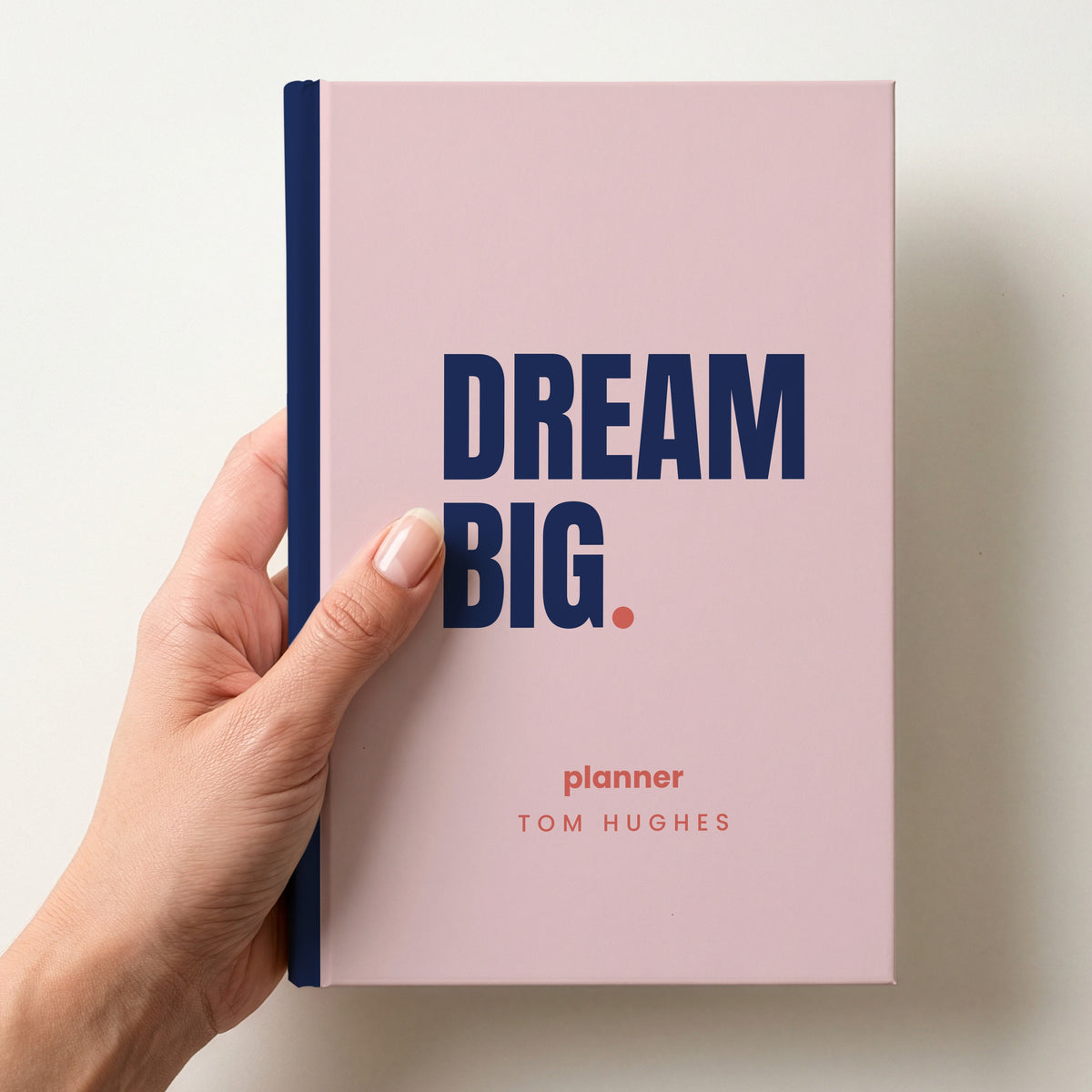 Hand holding a blush personalised notebook with 'DREAM BIG.' in navy and 'planner' and the name Tom Hughes below