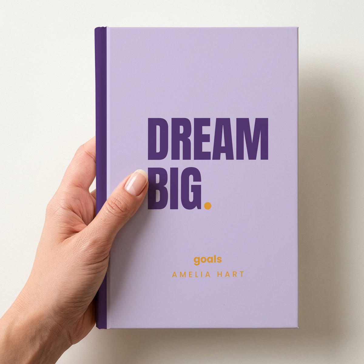 Hand holding a lilac personalised notebook with 'DREAM BIG.' in plum and 'goals' and the name Amelia Hart below