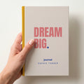 Hand holding a oat personalised notebook with 'DREAM BIG.' in coral and 'journal' and the name Sophie Turner below