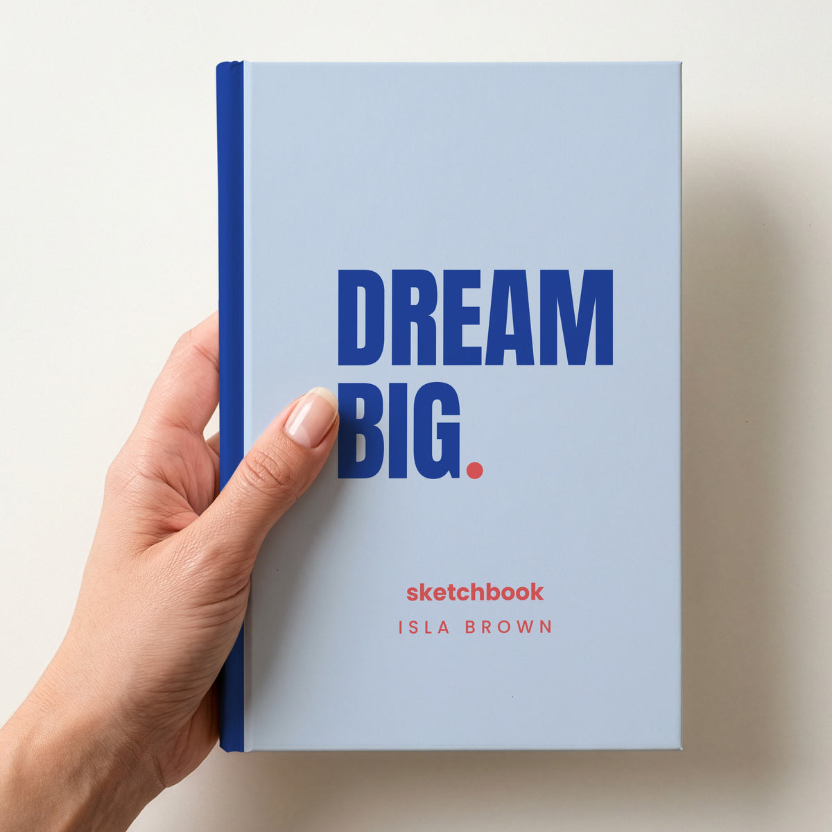 Hand holding a sky personalised notebook with 'DREAM BIG.' in cobalt and 'sketchbook' and the name Isla Brown below