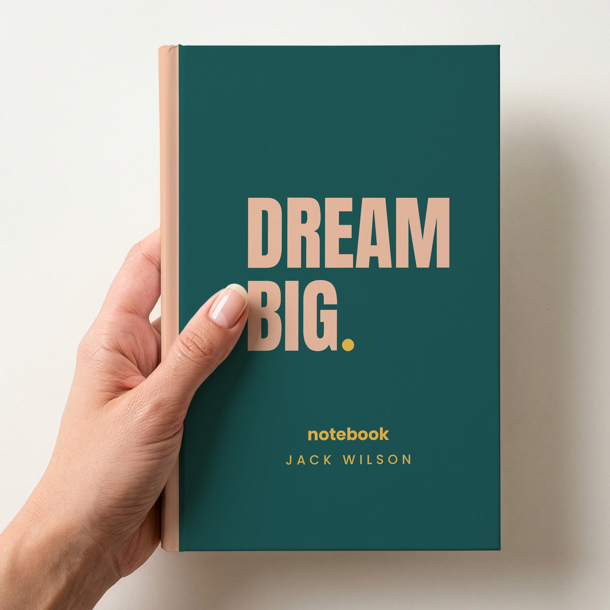 Hand holding a teal personalised notebook with 'DREAM BIG.' in peach and 'notebook' and the name Jack Wilson below