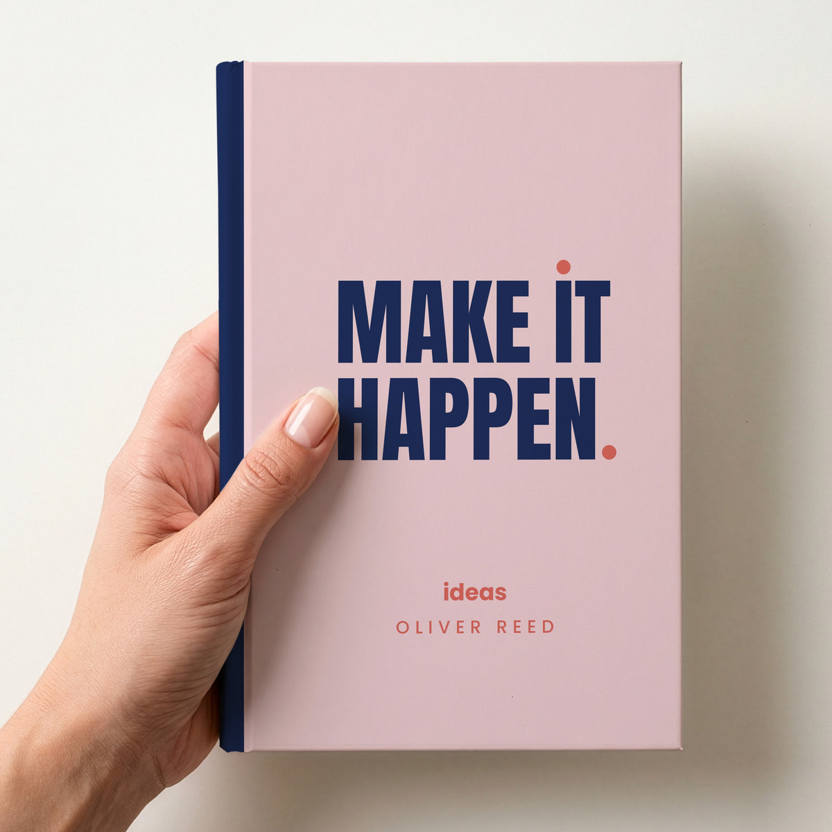 Hand holding a blush personalised notebook with 'MAKE IT HAPPEN.' in navy and 'ideas' and the name Oliver Reed below