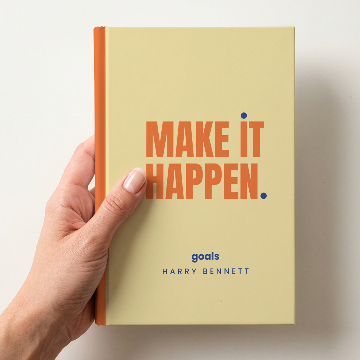 Hand holding a butter personalised notebook with 'MAKE IT HAPPEN.' in tangerine and 'goals' and the name Harry Bennett below