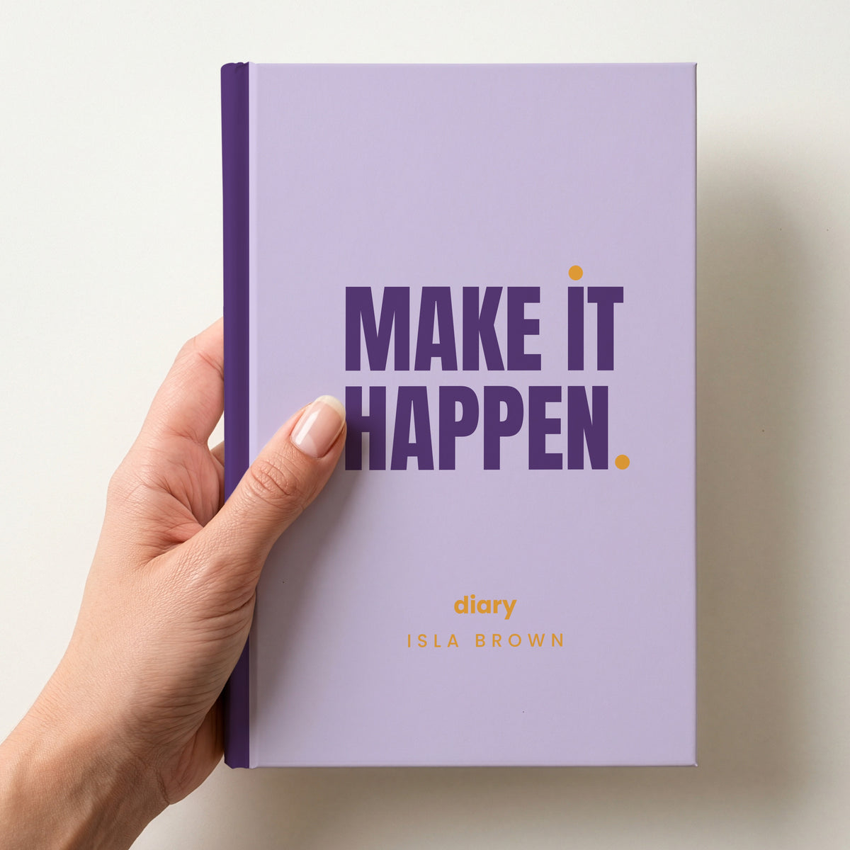 Hand holding a lilac personalised notebook with 'MAKE IT HAPPEN.' in plum and 'diary' and the name Isla Brown below