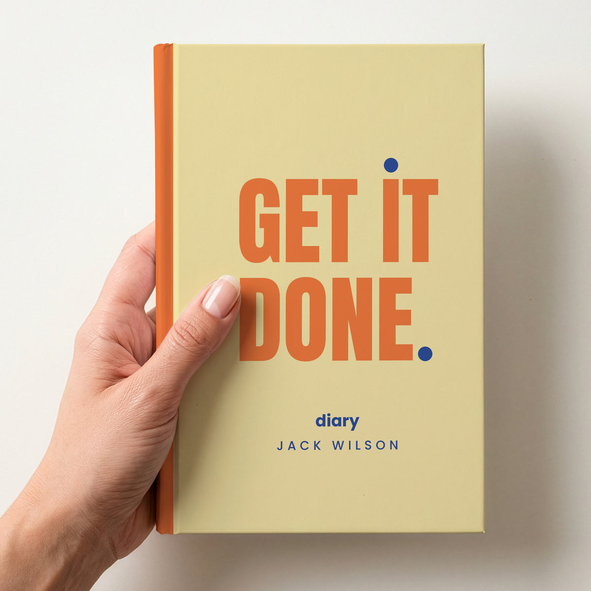 Hand holding a butter personalised notebook with 'GET IT DONE.' in tangerine and 'diary' and the name Jack Wilson below