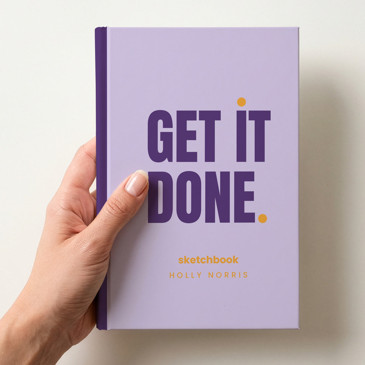 Hand holding a lilac personalised notebook with 'GET IT DONE.' in plum and 'sketchbook' and the name Holly Norris below