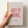 Hand holding a oat personalised notebook with 'GET IT DONE.' in coral and 'ideas' and the name Amelia Hart below