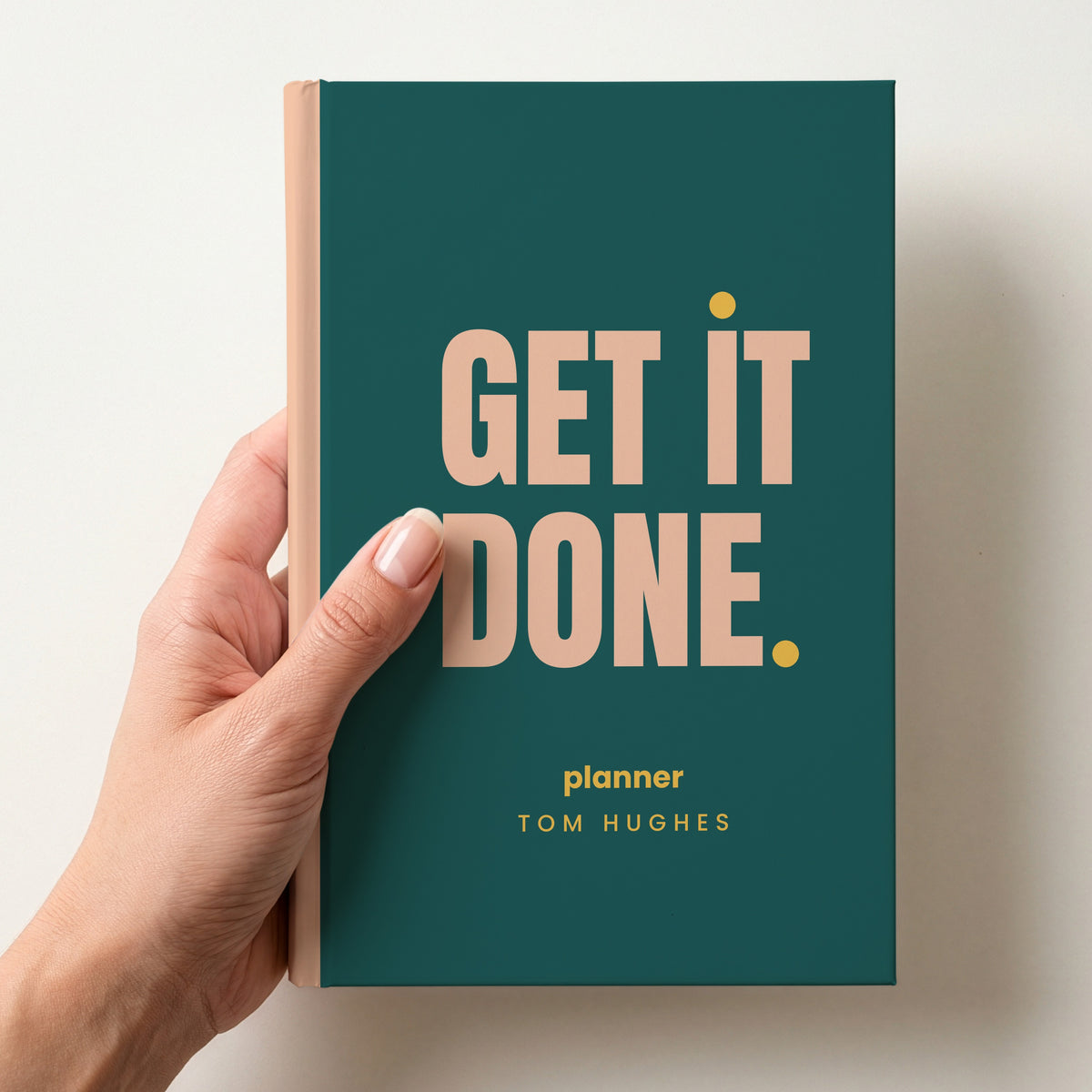 Hand holding a teal personalised notebook with 'GET IT DONE.' in peach and 'planner' and the name Tom Hughes below