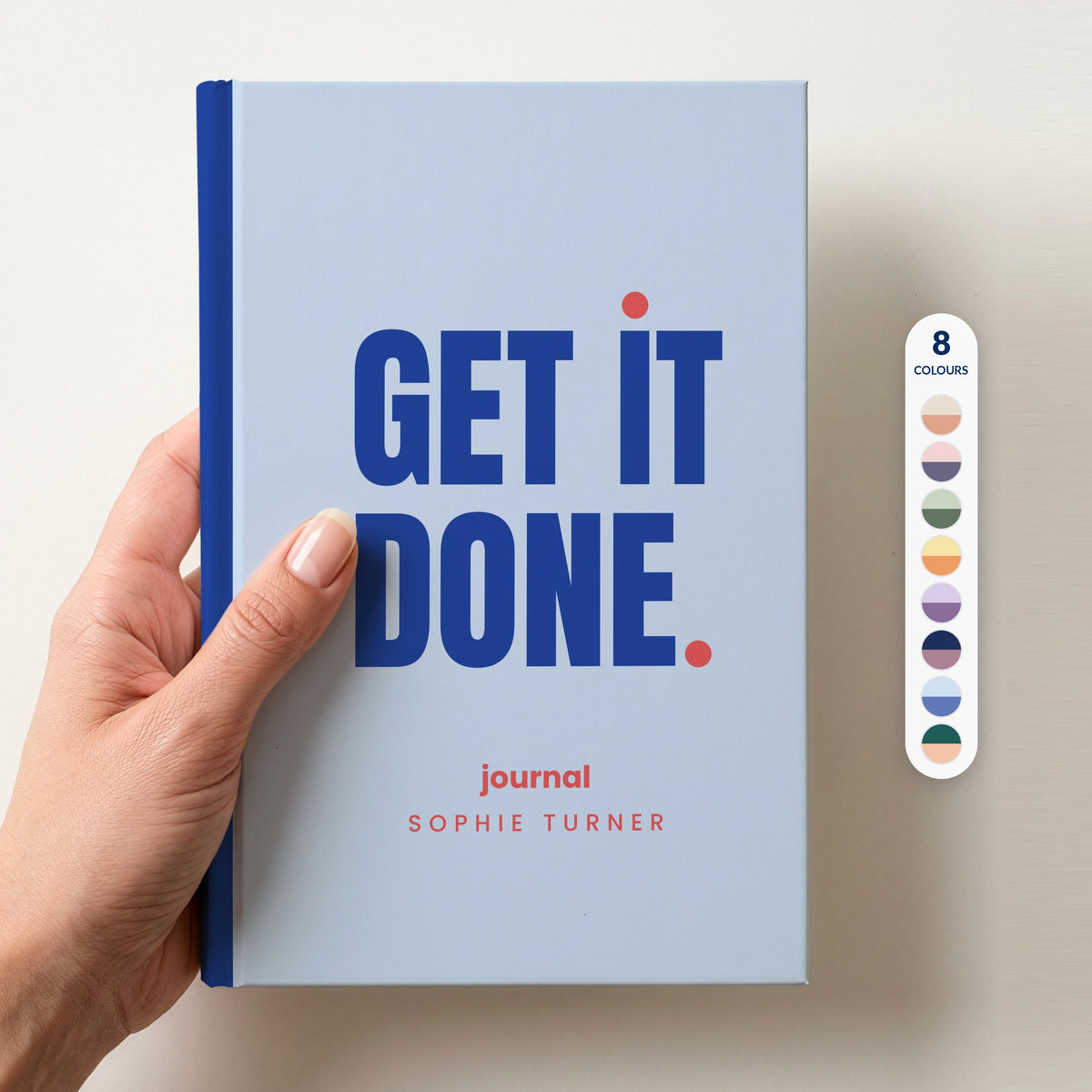 Hand holding a sky personalised notebook with 'GET IT DONE.' in cobalt and 'journal' and the name Sophie Turner below, beside a column of 8 colour swatches showing all 8 colourways