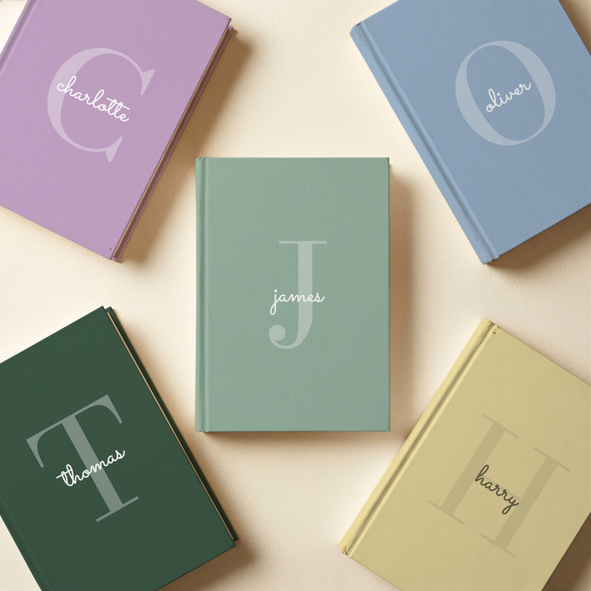 Five personalised initial journals in powder blue, lavender, forest green, butter and sage with names oliver, charlotte, thomas, harry and james