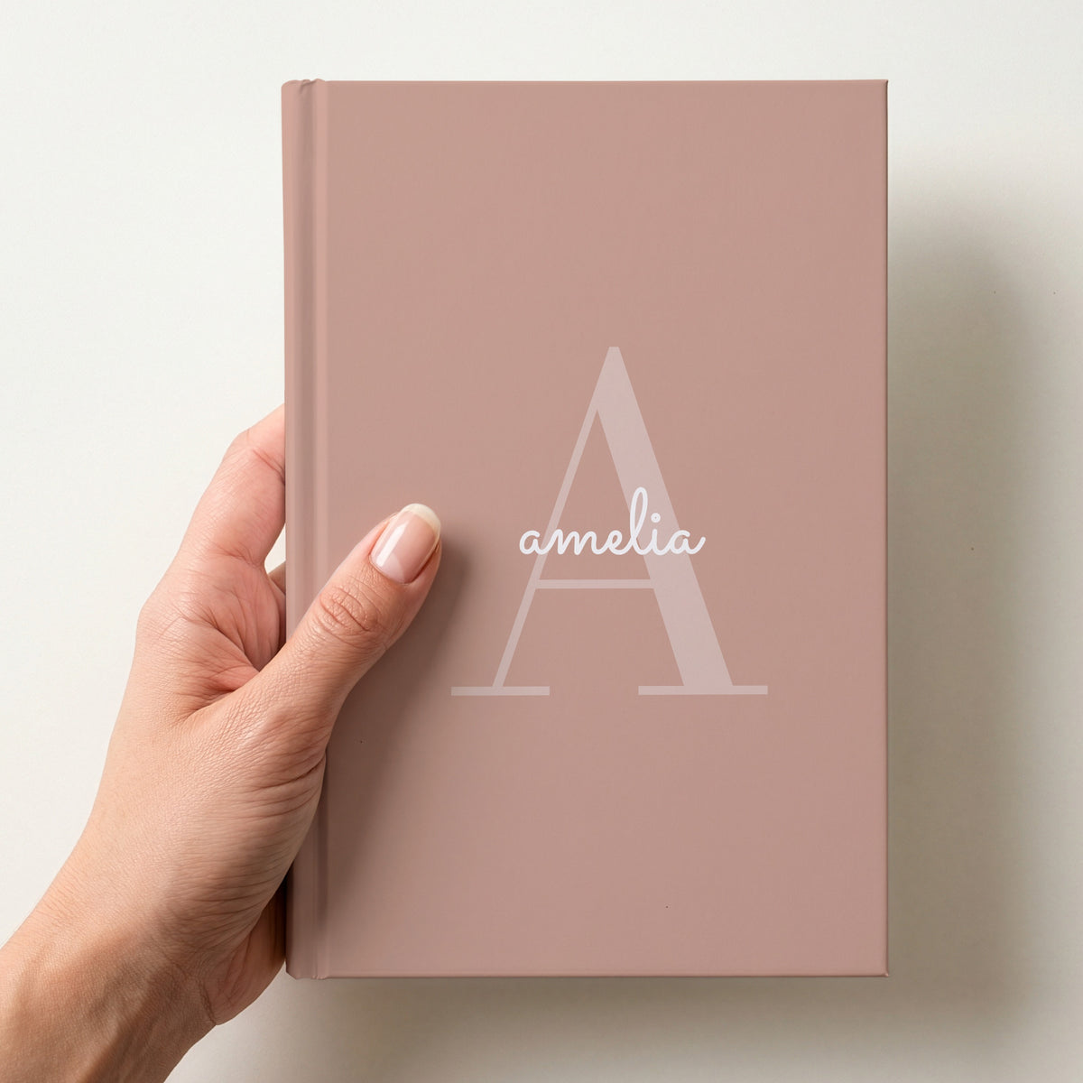 Hand holding a blush personalised journal with a large A initial and the name amelia in script