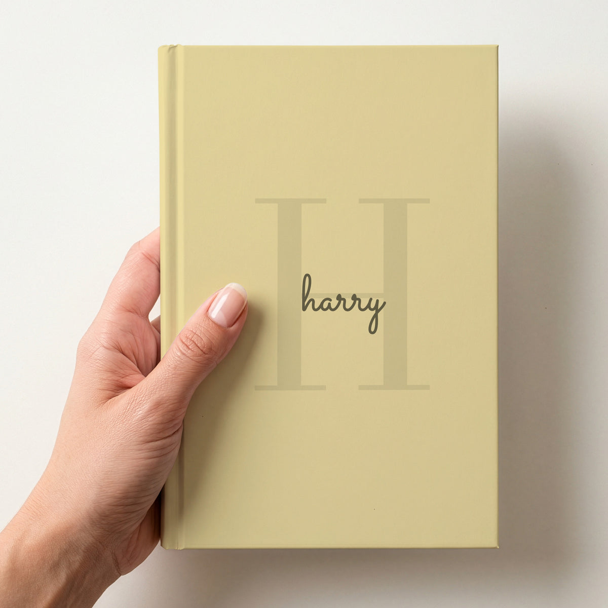 Hand holding a butter personalised journal with a large H initial and the name harry in script