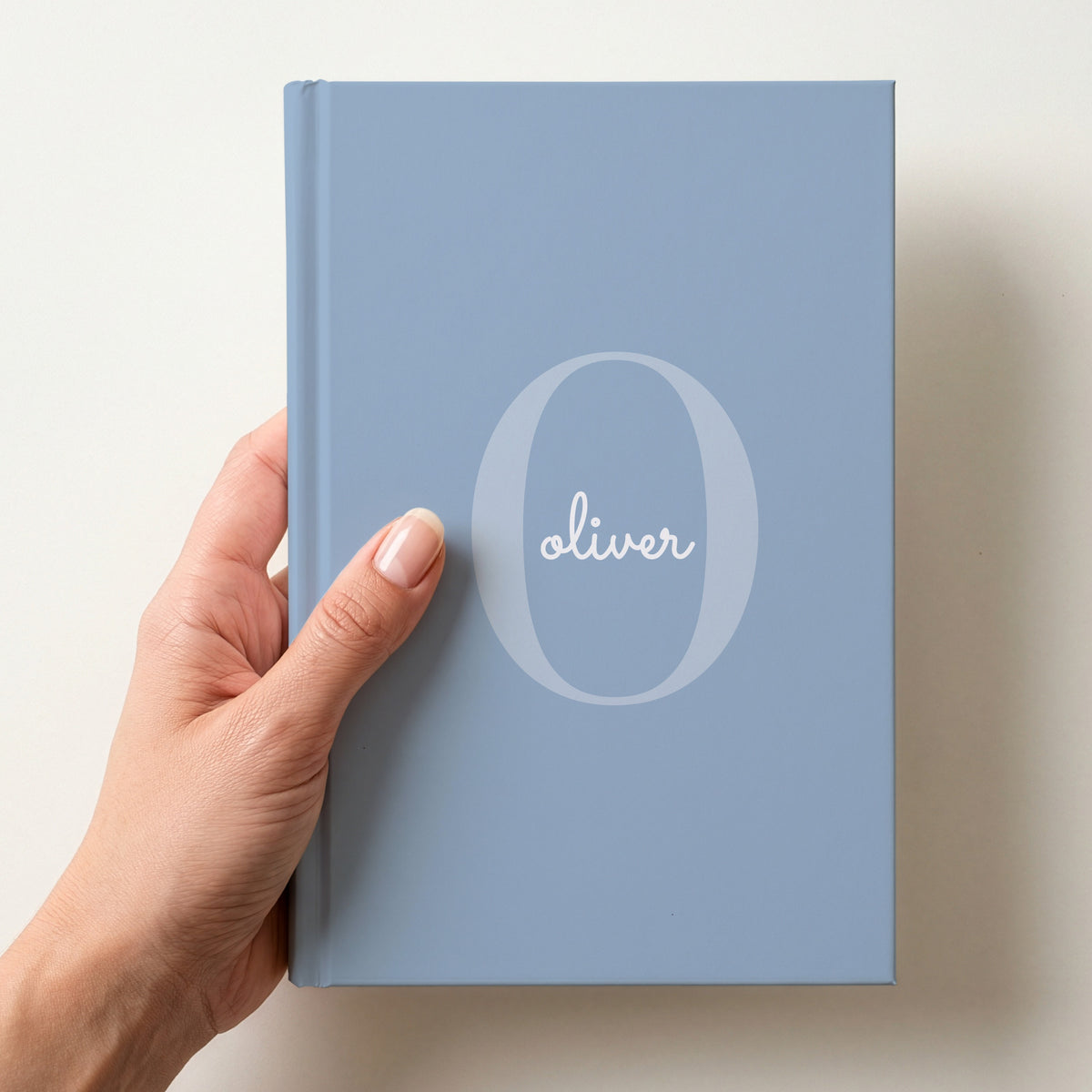 Hand holding a powder blue personalised journal with a large O initial and the name oliver in script