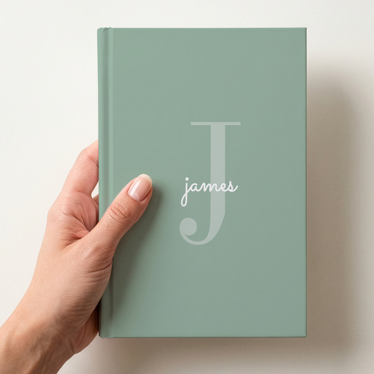 Hand holding a sage personalised journal with a large J initial and the name james in script