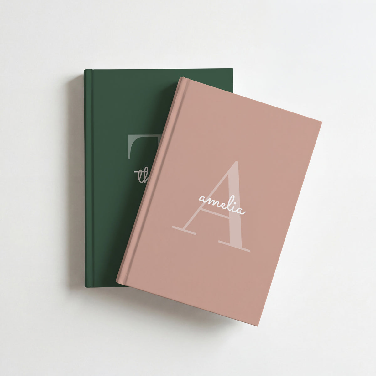 Two personalised initial journals, blush for amelia on top of forest green for thomas