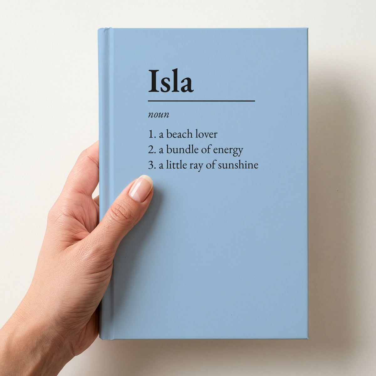 Hand holding a sky blue personalised notebook with a dictionary definition of Isla: a beach lover, a bundle of energy, a little ray of sunshine