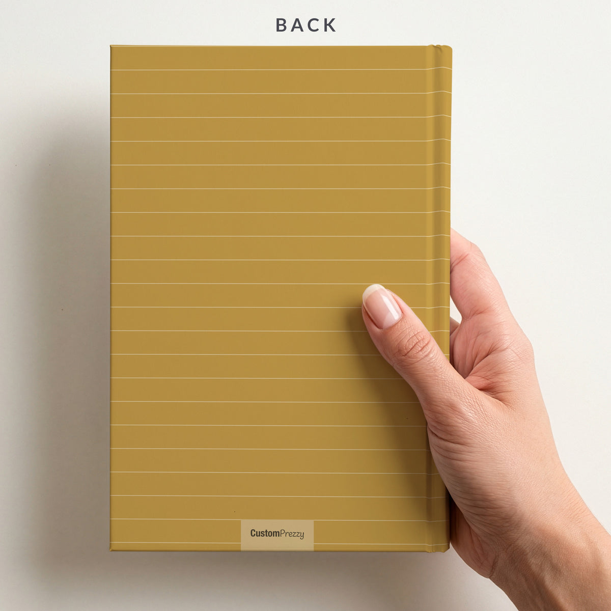 Back of the mustard notebook held in a hand, with the Custom Prezzy wordmark at the foot