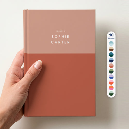 Hand holding a terracotta colour block notebook with RECIPES and the name Sophie Carter in spaced capitals, beside a column of 10 colour swatches showing all 10 colourways
