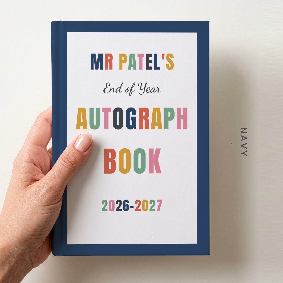 Hand holding a personalised teacher autograph book with a navy border, reading MR PATEL'S, End of Year AUTOGRAPH BOOK and 2026–2027