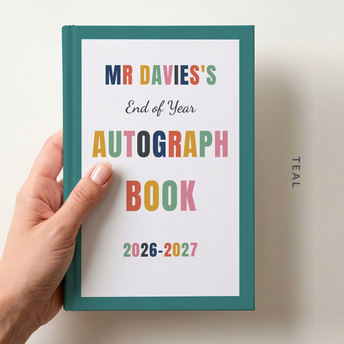 Hand holding a personalised teacher autograph book with a teal border, reading MR DAVIES'S, End of Year AUTOGRAPH BOOK and 2026–2027