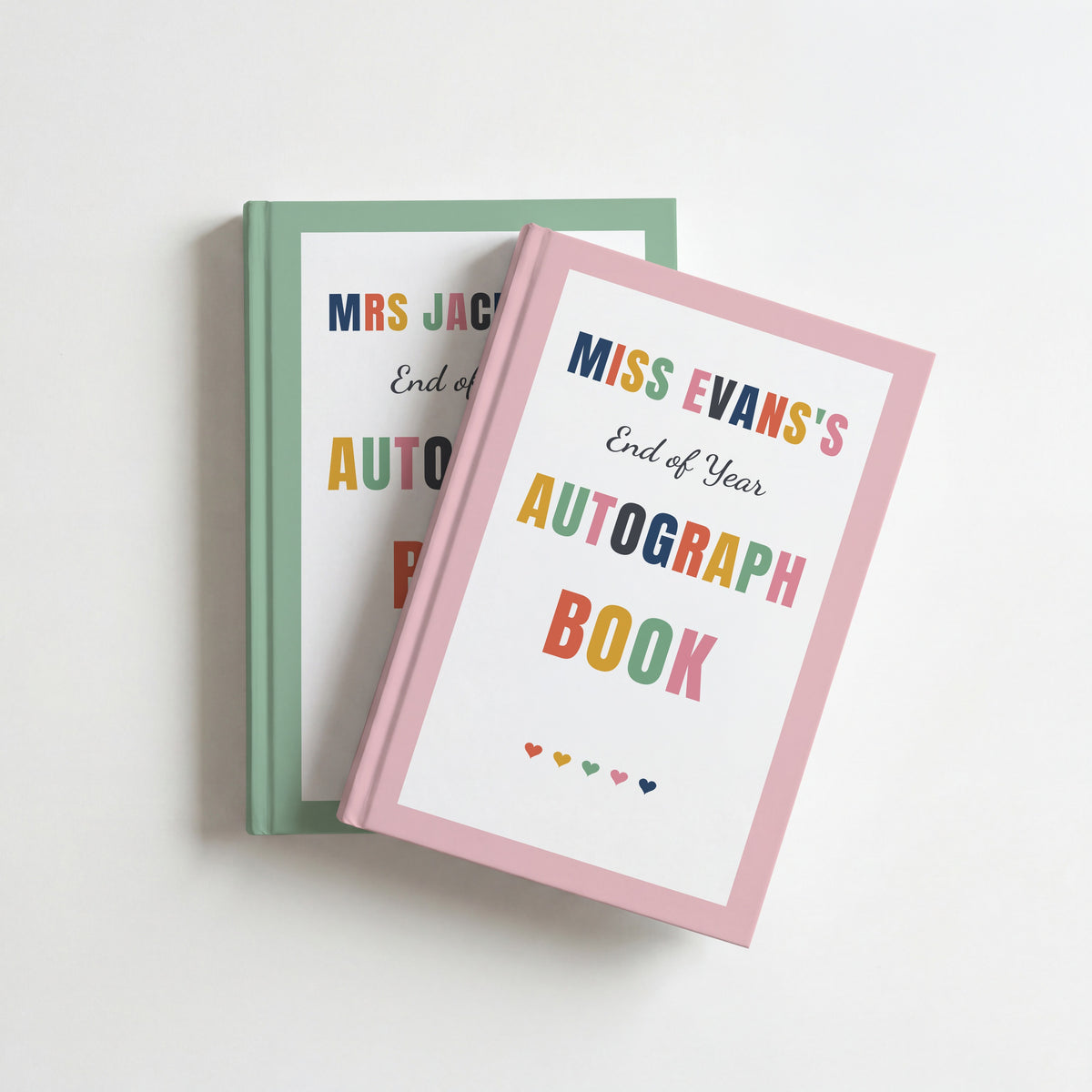 Two teacher autograph books, blush pink for Miss Evans on top of sage green for Mrs Jackson, both with a row of hearts